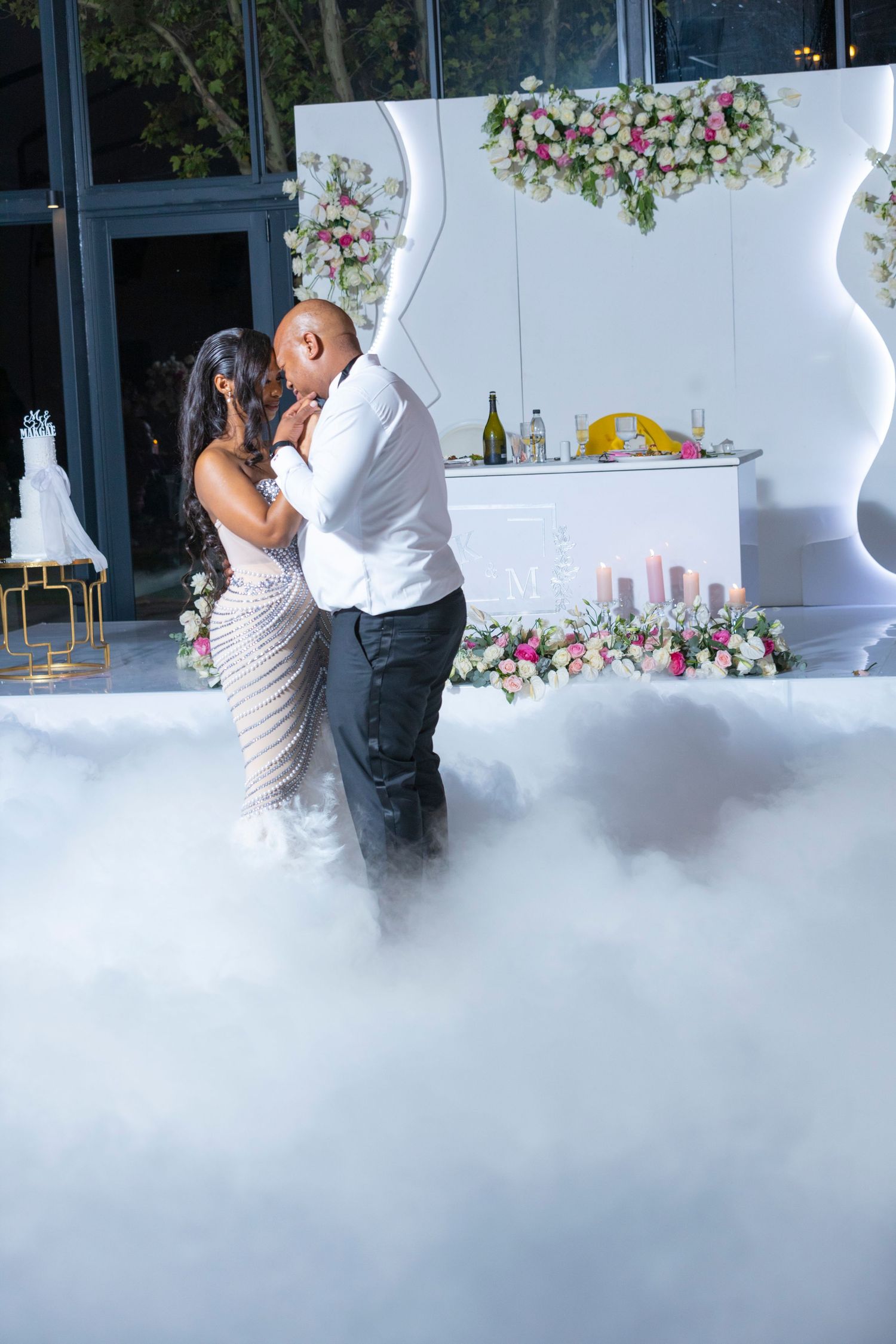 Newlyweds share their first dance surrounded by dramatic fog on an elegantly decorated dance floor.