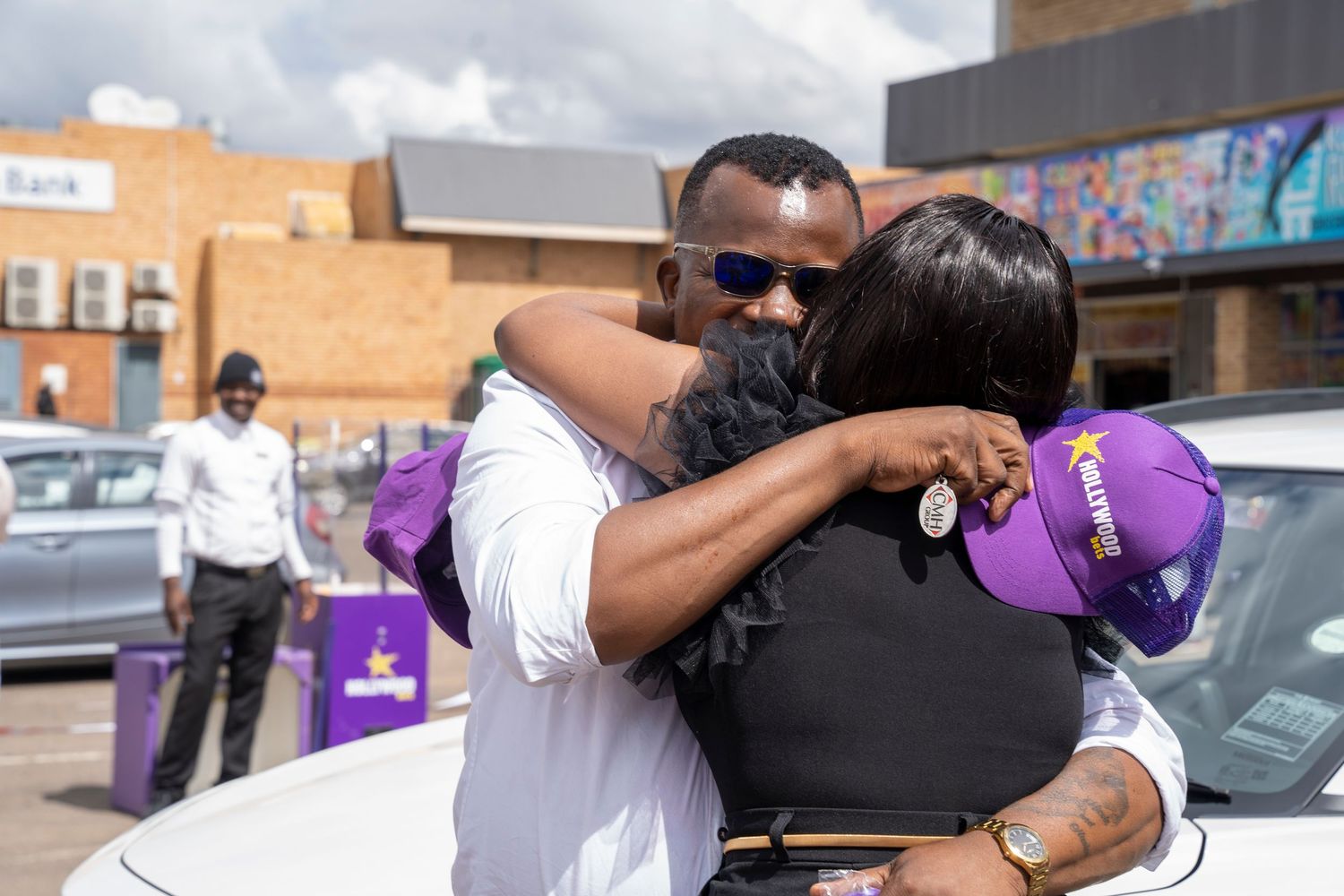 Man and woman share a warm embrace at an outdoor Hollywoodbets prize-giving event.
