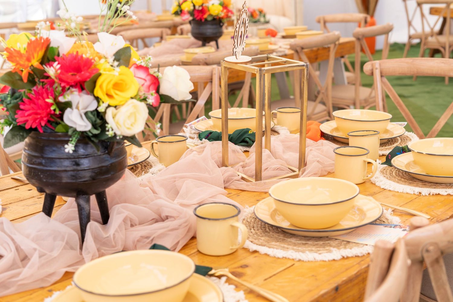 Elegant wedding table decor featuring yellow dinnerware, colorful flowers in a black pot, and tulle runner.
