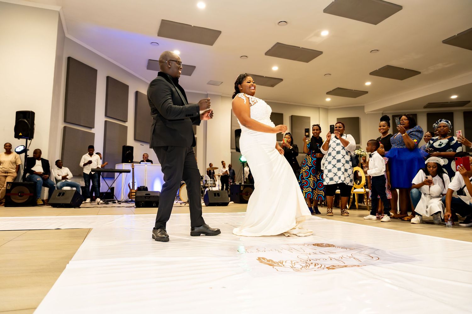 Bride and groom dancing together at wedding reception with guests seated in background.