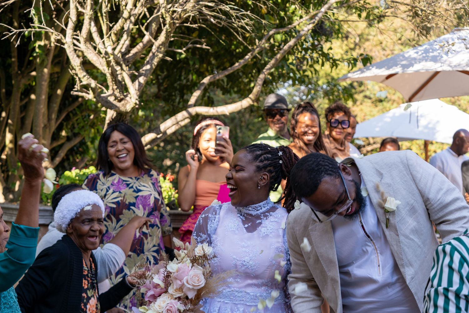 Joyful bride in white dress celebrating with guests outdoors, confetti flying at wedding reception.