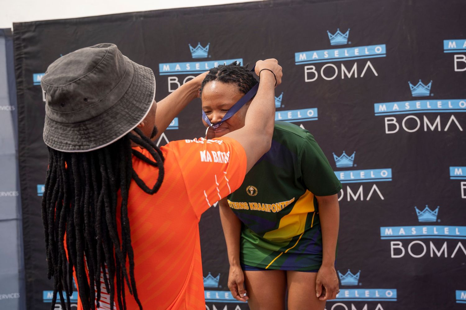 A person places a medal around a young female athlete's neck at a Maselelo Boma event.