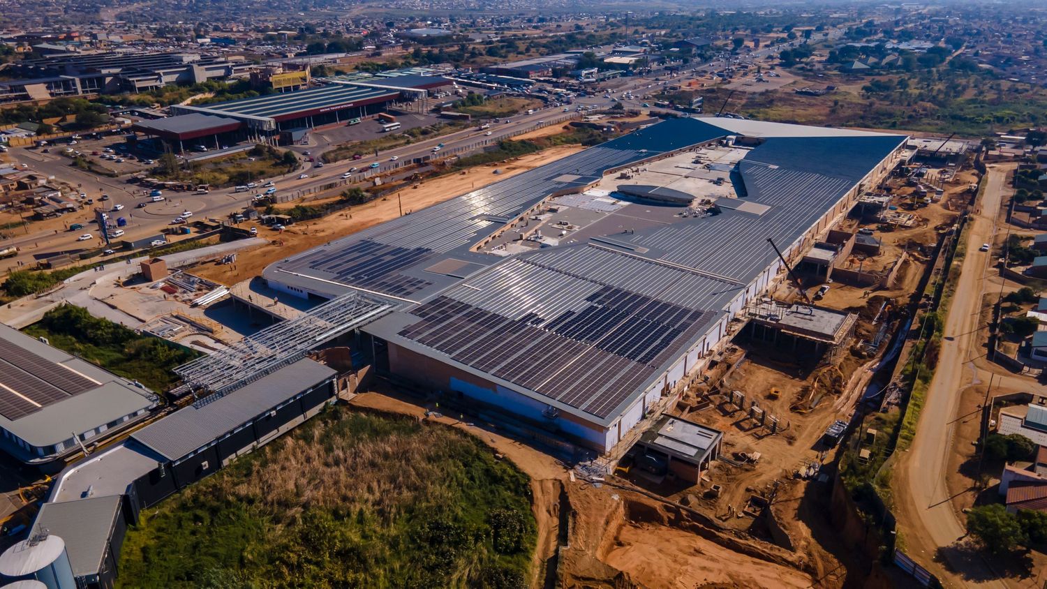 Aerial view of a large warehouse facility with solar panels under construction in an urban setting.