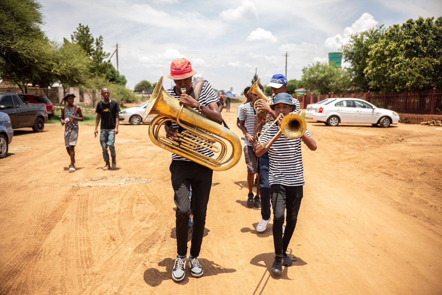 Musicians playing brass instruments on a dirt road during an outdoor African cultural celebration.