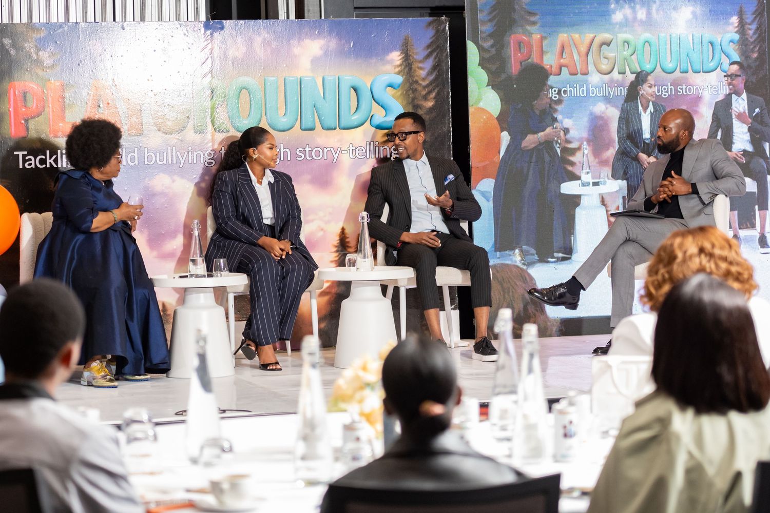 Panel discussion at Playgrounds event with four speakers on stage before an audience at a formal dining setting.