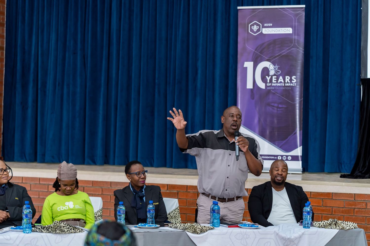 Man addresses panel and audience at a 10 Years community foundation indoor event.
