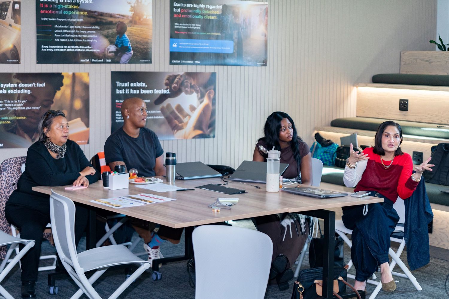 Four diverse professionals engaged in a collaborative discussion around a modern office table with laptops and water bottles.