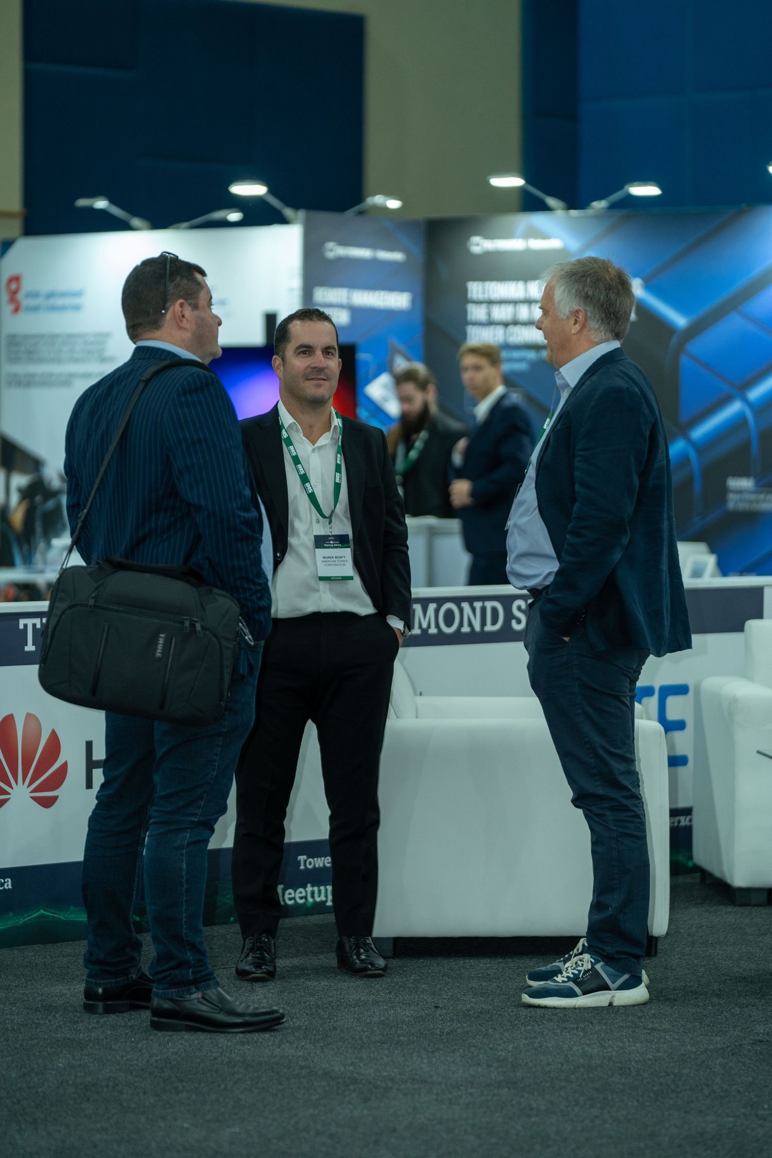 Three businessmen in suits engage in conversation at the TowerXchange Meetup Africa exhibition floor.