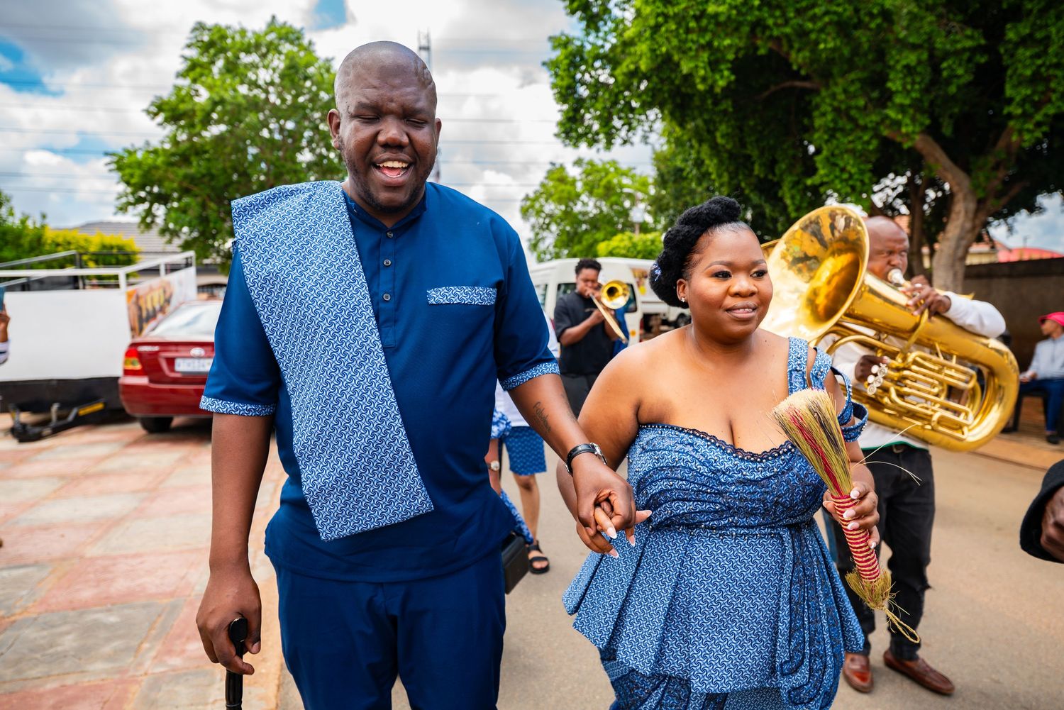 Couple in matching blue traditional African attire holding hands outdoors at a festive celebration.