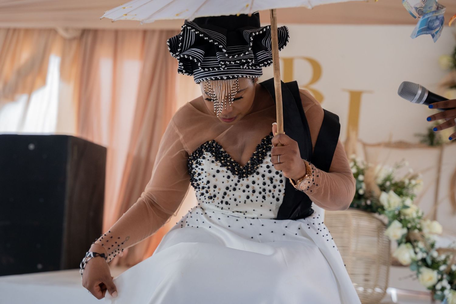 Bride in black and white beaded wedding gown holding decorative umbrella at traditional African wedding ceremony.