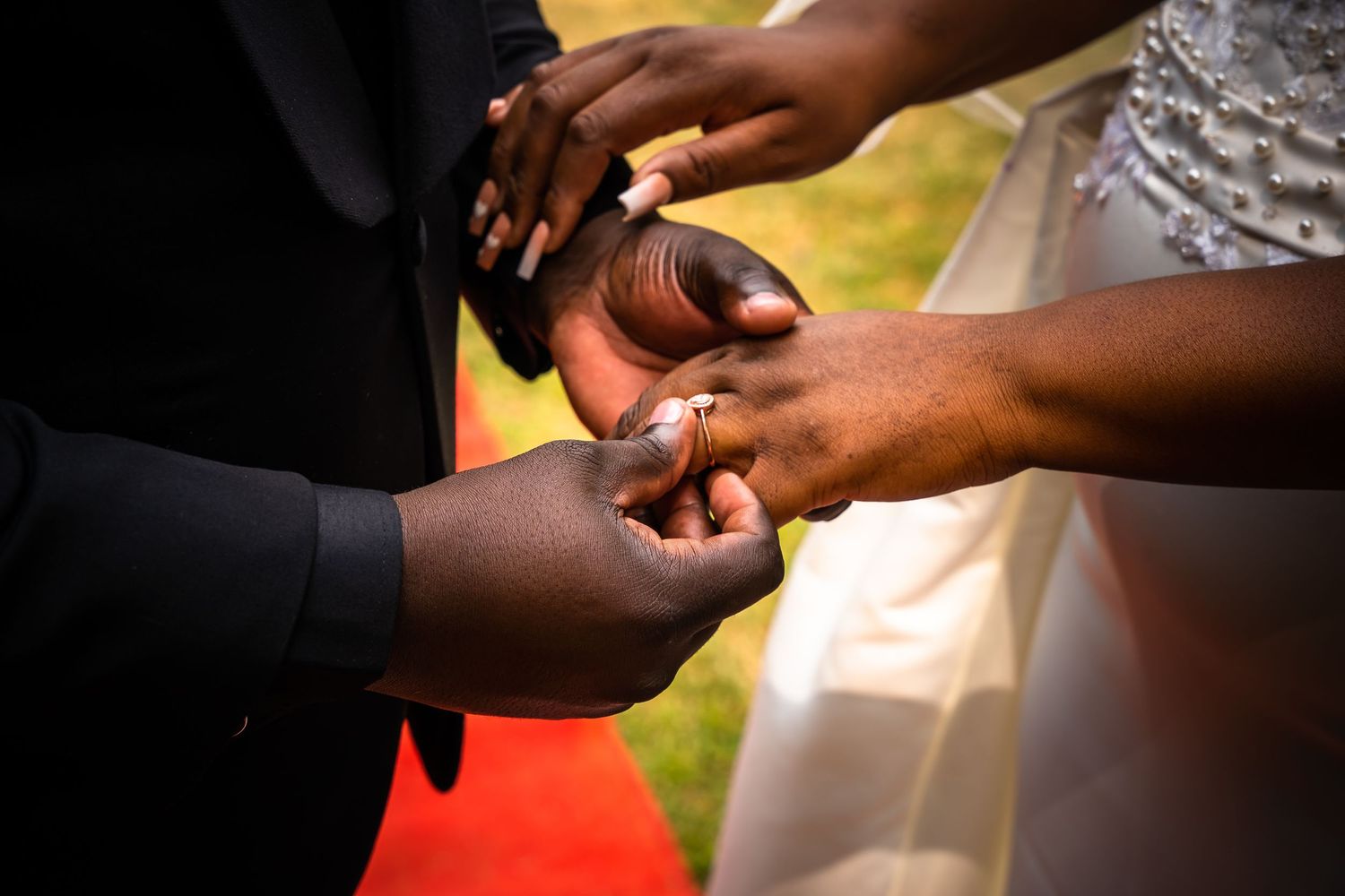 Close-up of groom placing wedding ring on brides finger during outdoor ceremony.