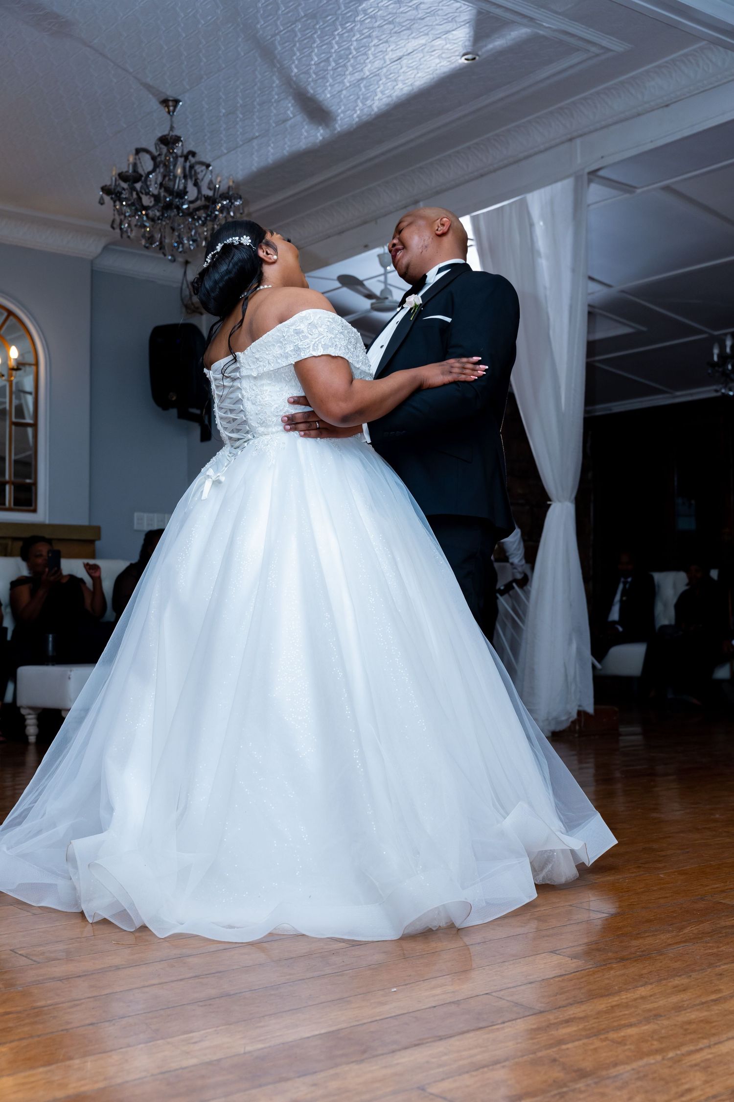 Bride and groom sharing their first dance in elegant reception venue with chandelier overhead.