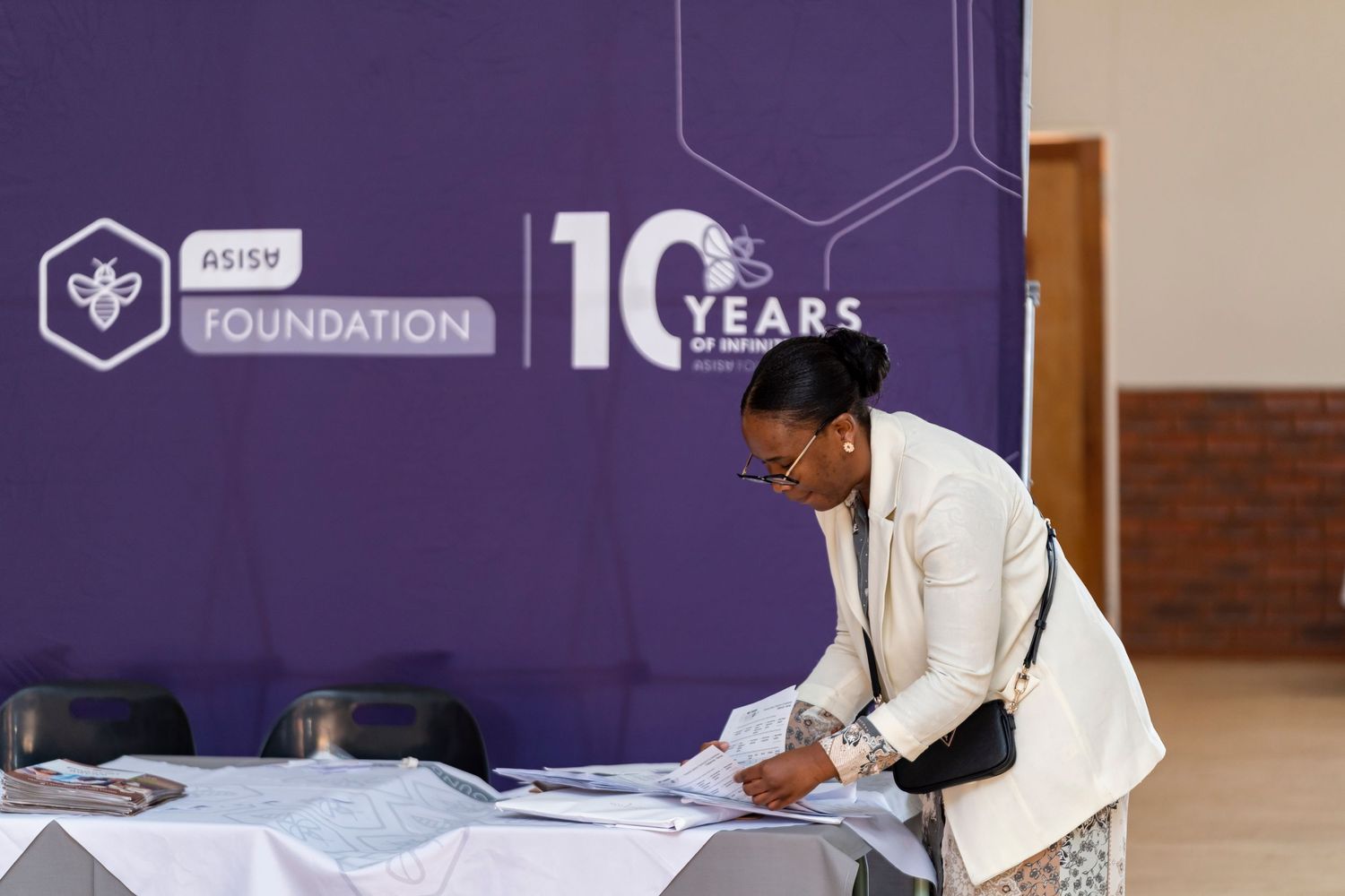 Woman in white blazer reviews documents at ASISA Foundation 10 Years anniversary event registration table.