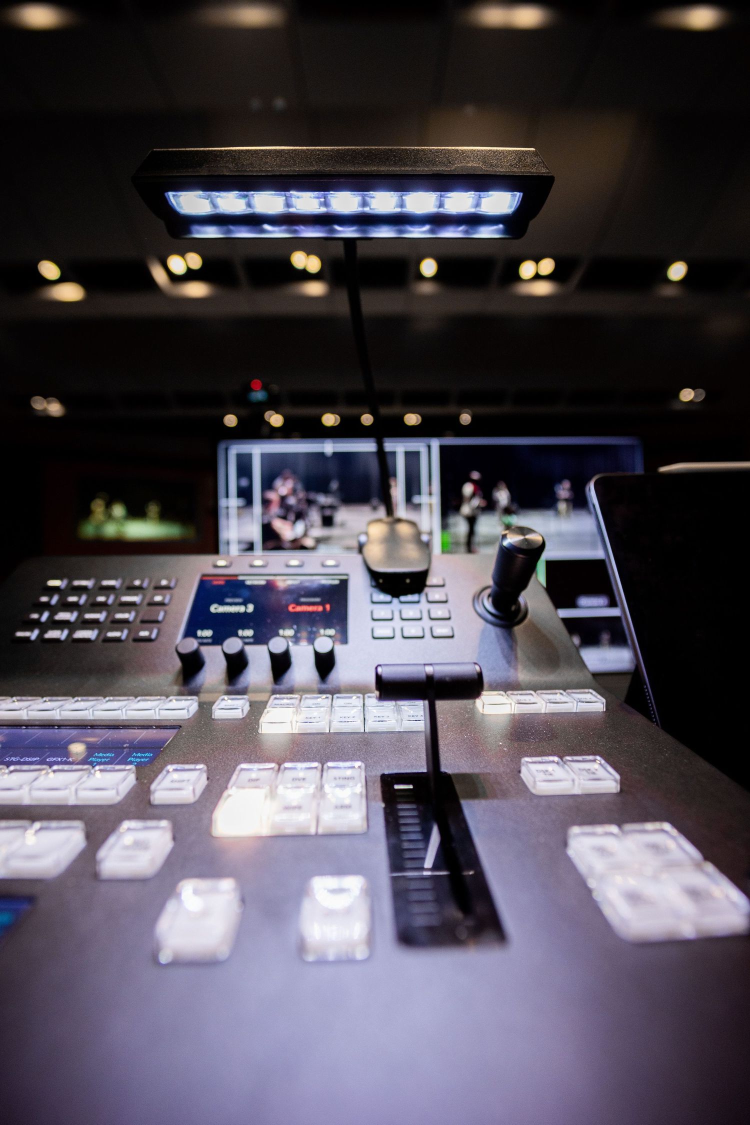 Professional broadcast control panel with joystick, monitors, and illuminated buttons in a dark production studio.