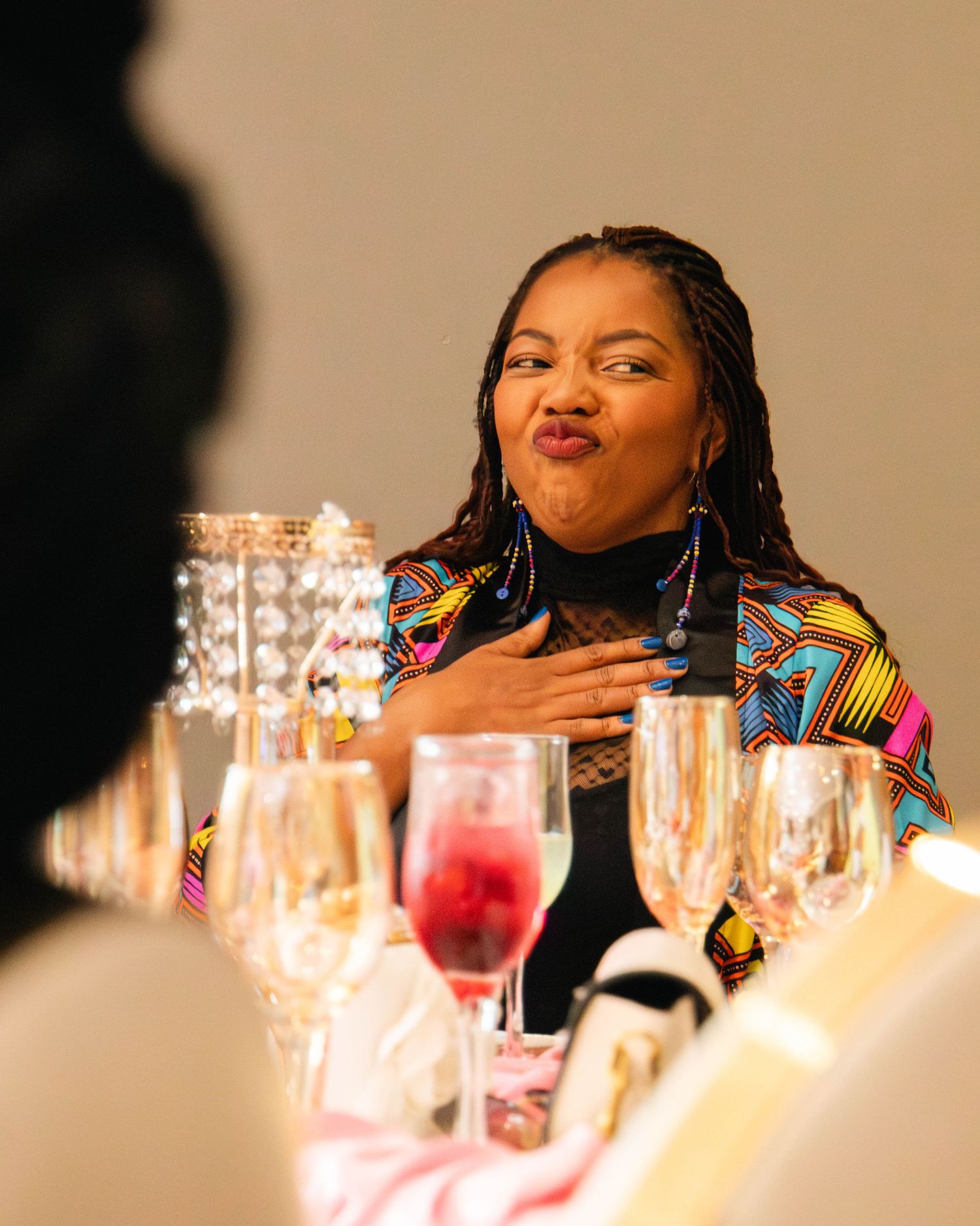 Woman in colorful jacket making a kissy face at a elegant dinner table with crystal glasses and champagne.