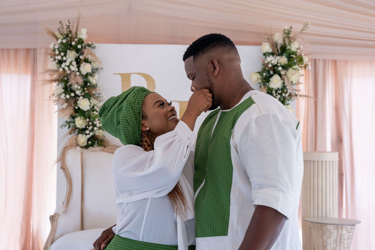 Couple in green and white traditional African attire sharing romantic moment at wedding ceremony.