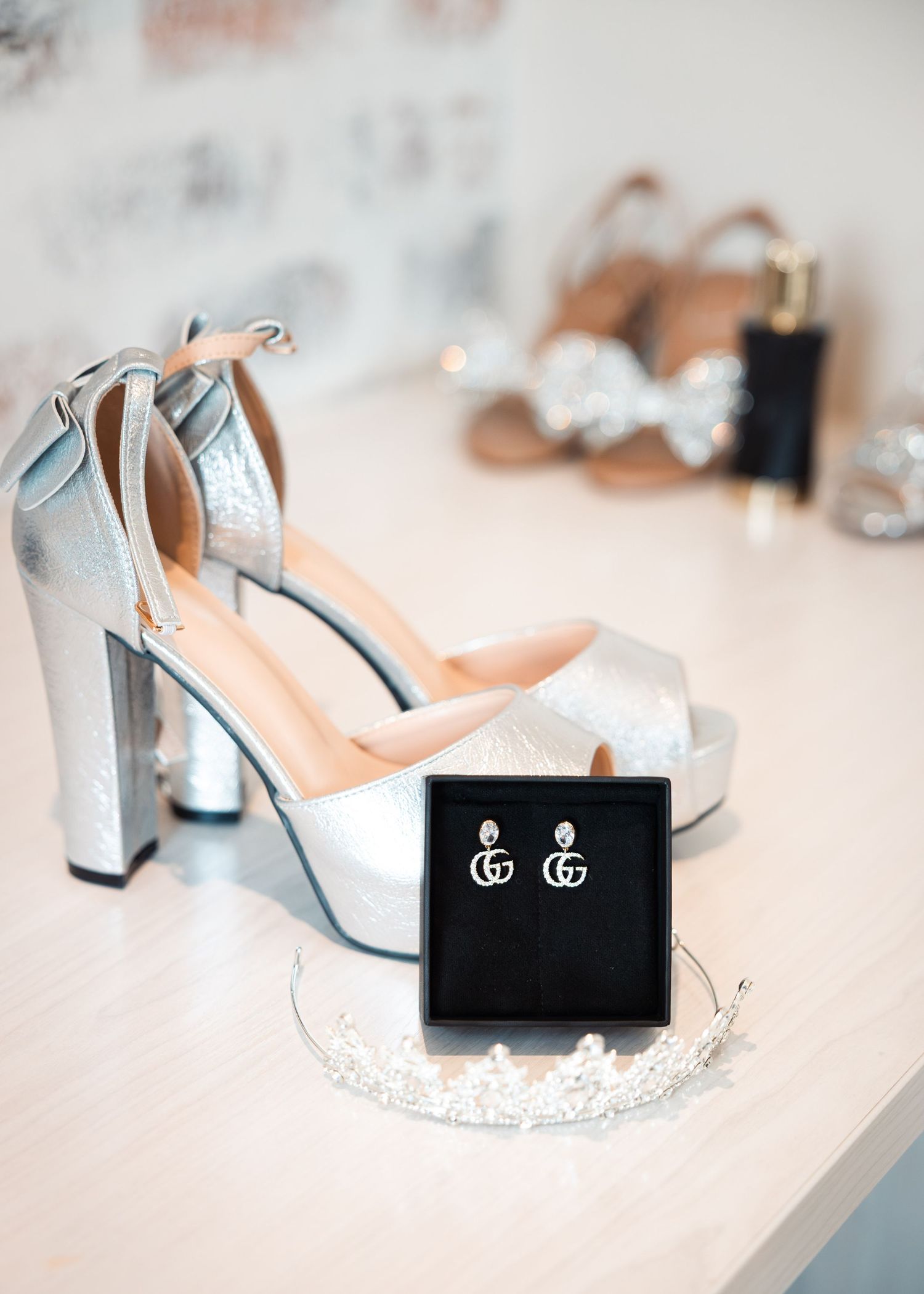 Silver platform heels with Gucci earrings in a black box and a crystal tiara displayed on a white surface.