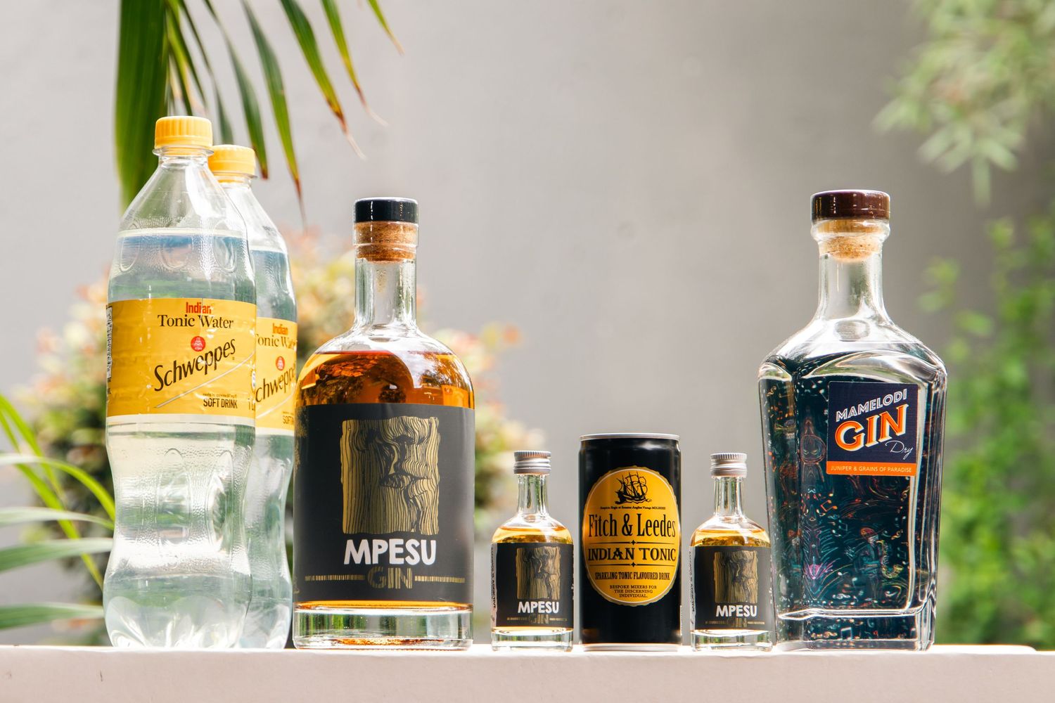 Schweppes tonic water, MPESU whiskey bottle, MPESU can, Pub & Lime tonic, and gin bottle displayed on a table.