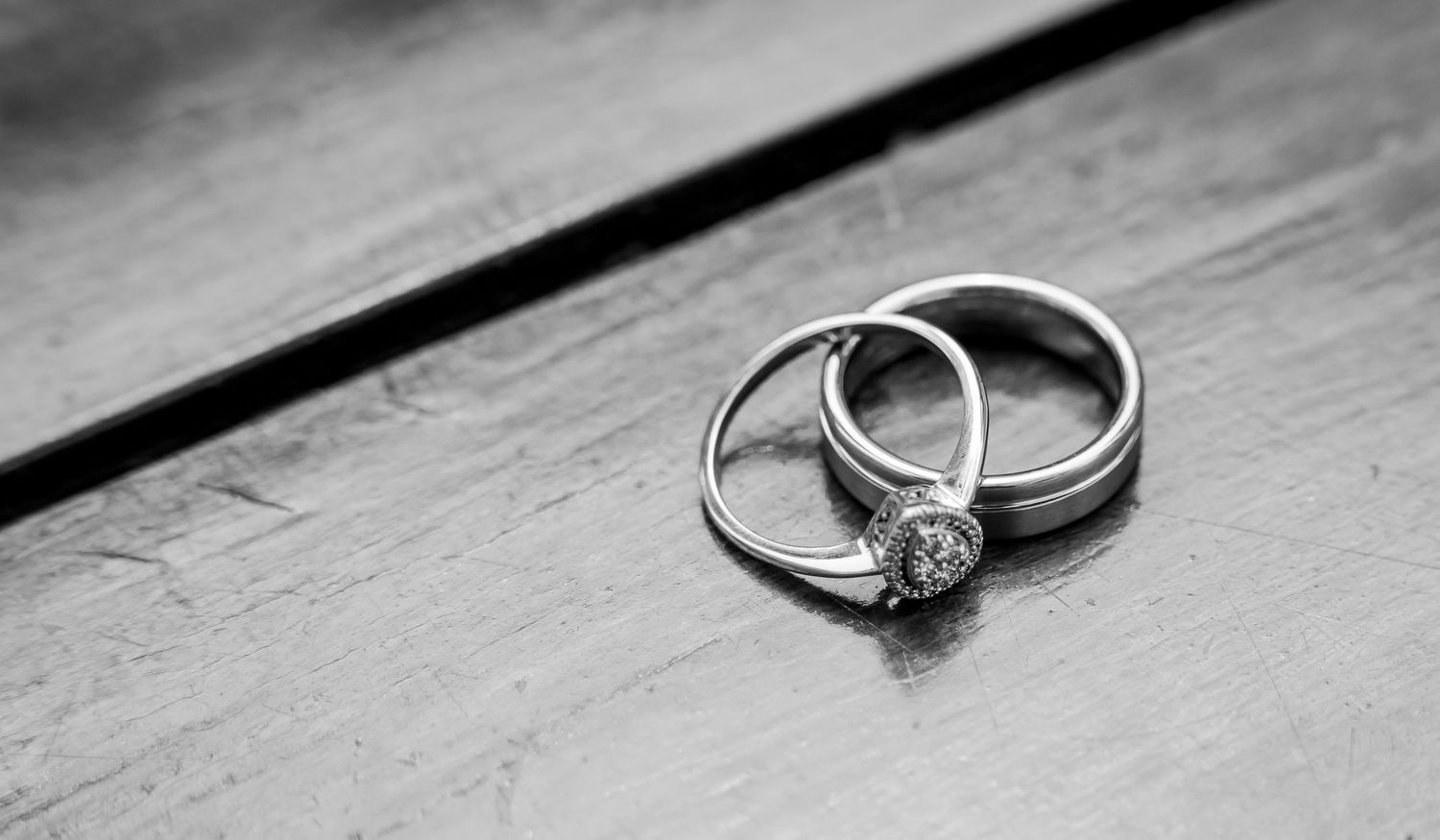 Black and white close-up of wedding rings, an engagement ring with diamond and a plain band, on wood.