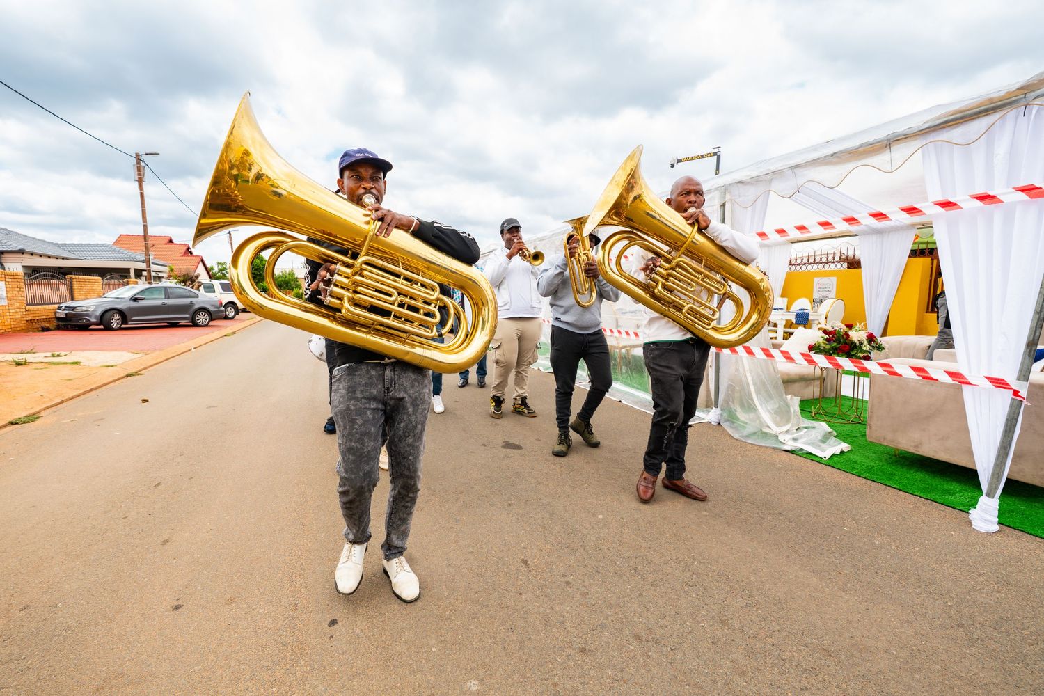 Two musicians playing brass tubas on a street during a vibrant outdoor cultural celebration.
