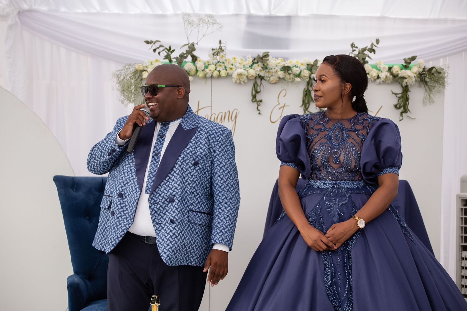 Couple in blue formal and traditional African attire seated together at an elegant wedding reception.