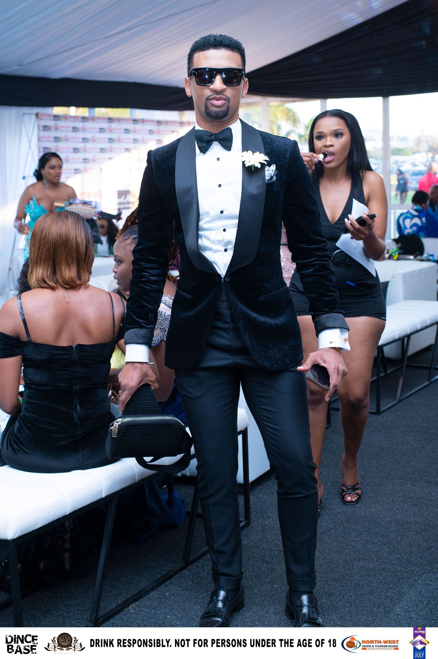 Elegant man in black velvet tuxedo with bow tie and boutonniere at a formal outdoor event.
