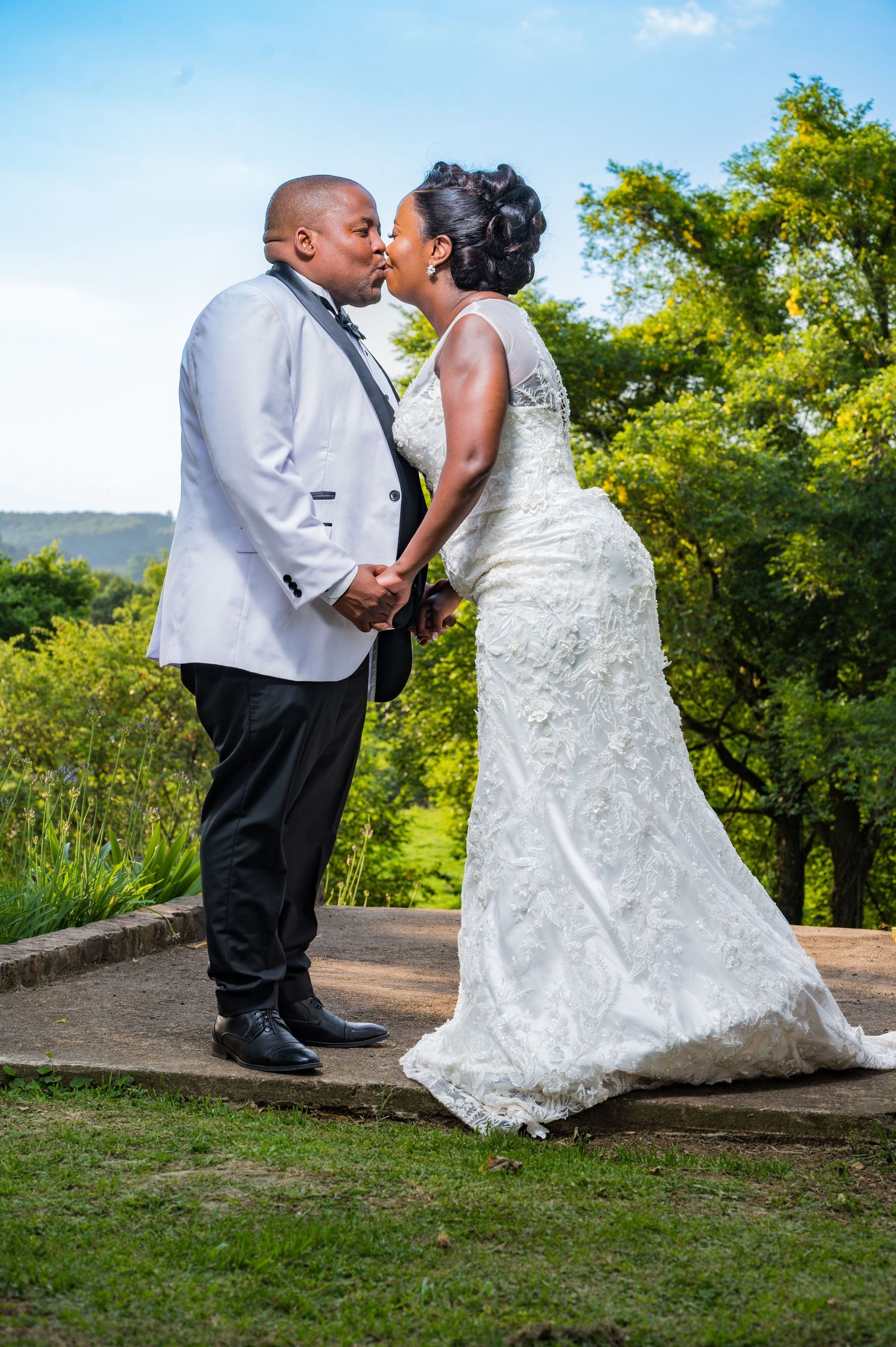 Bride and groom sharing a romantic kiss outdoors on their wedding day surrounded by greenery.