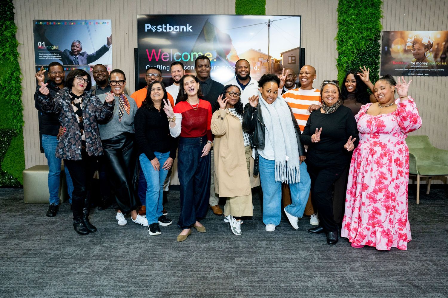A diverse group of smiling people posing together in front of a Postbank welcome sign at a corporate event.