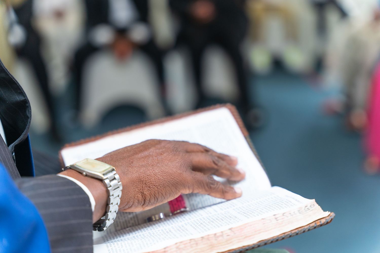 Close-up of a man in a suit reading from an open Bible during a wedding ceremony.