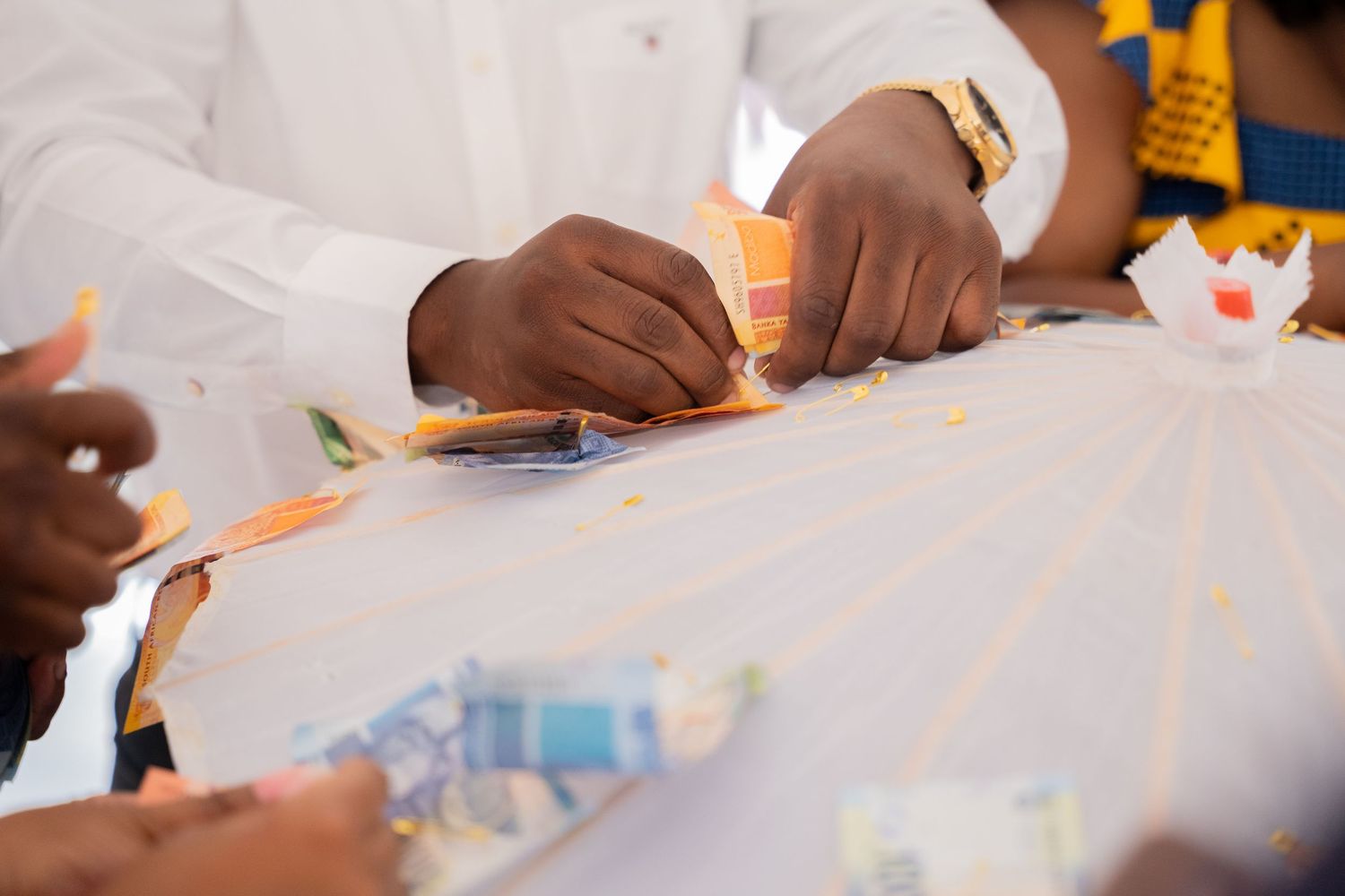 Hands pinning colorful banknotes onto decorative umbrella at traditional African wedding money dance.