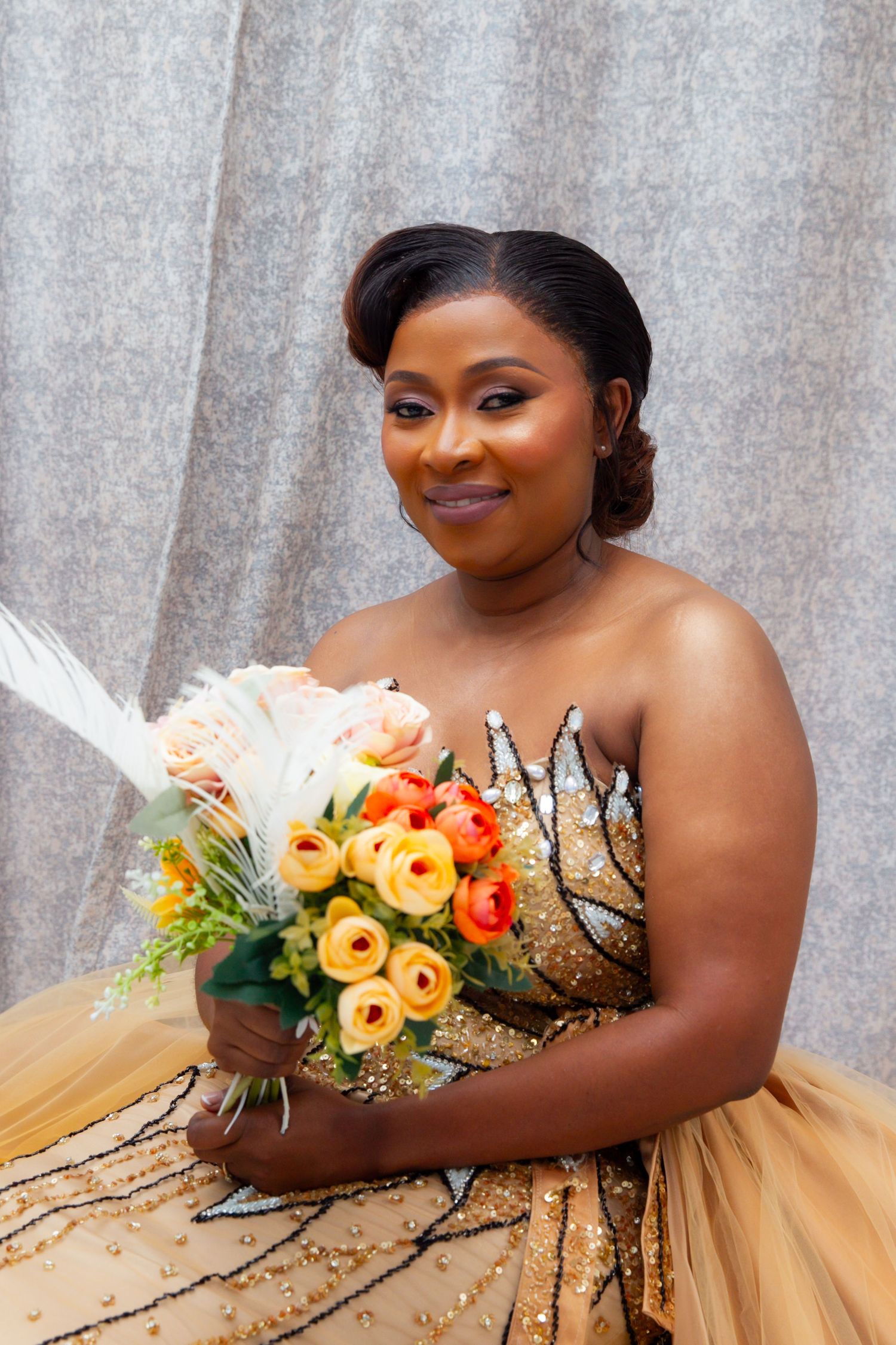 Smiling bride in gold beaded strapless gown holding a colorful bouquet of roses and lilies.