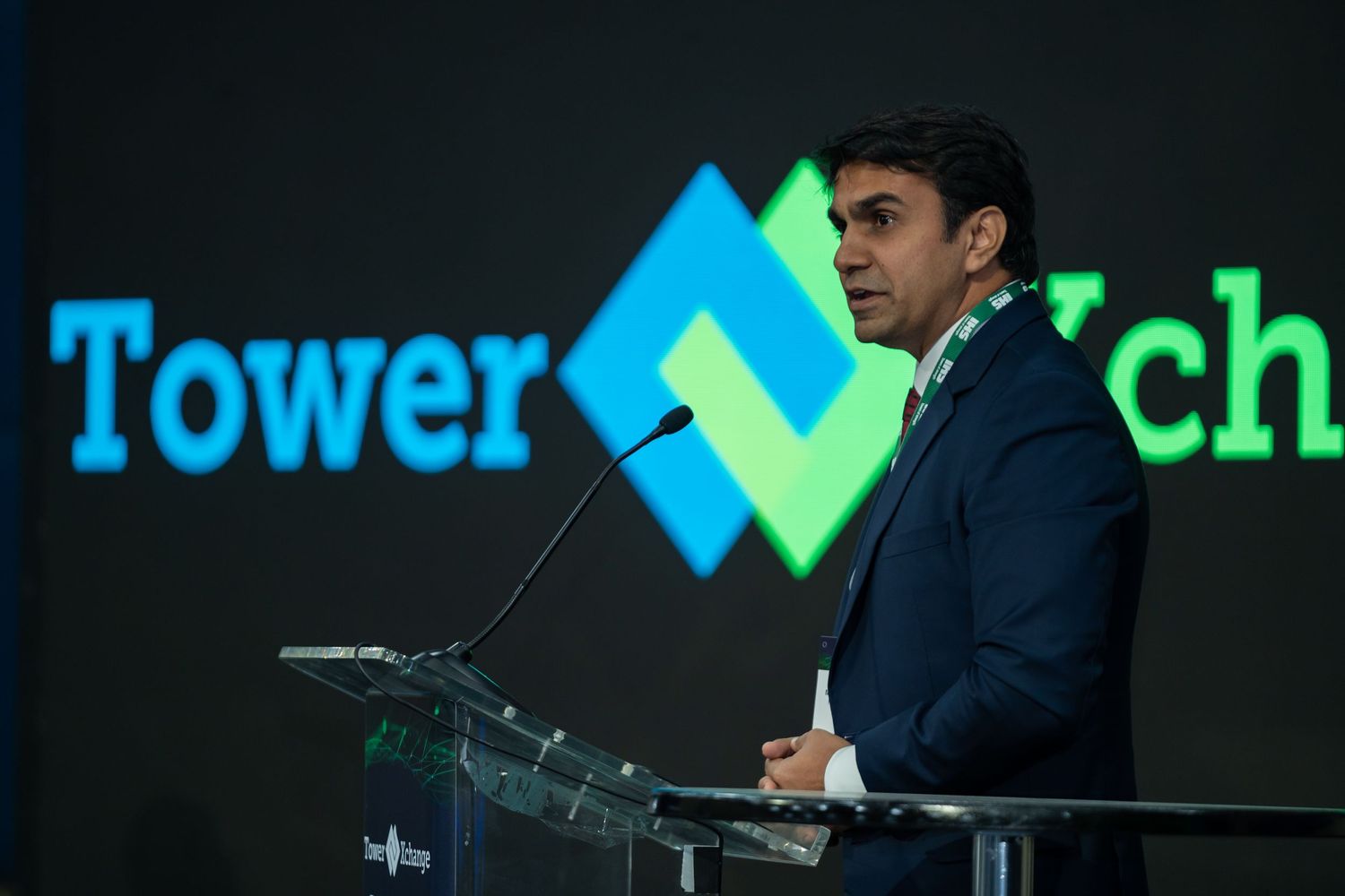 A young man in a navy blazer delivers a speech at a TowerXchange branded podium on stage.