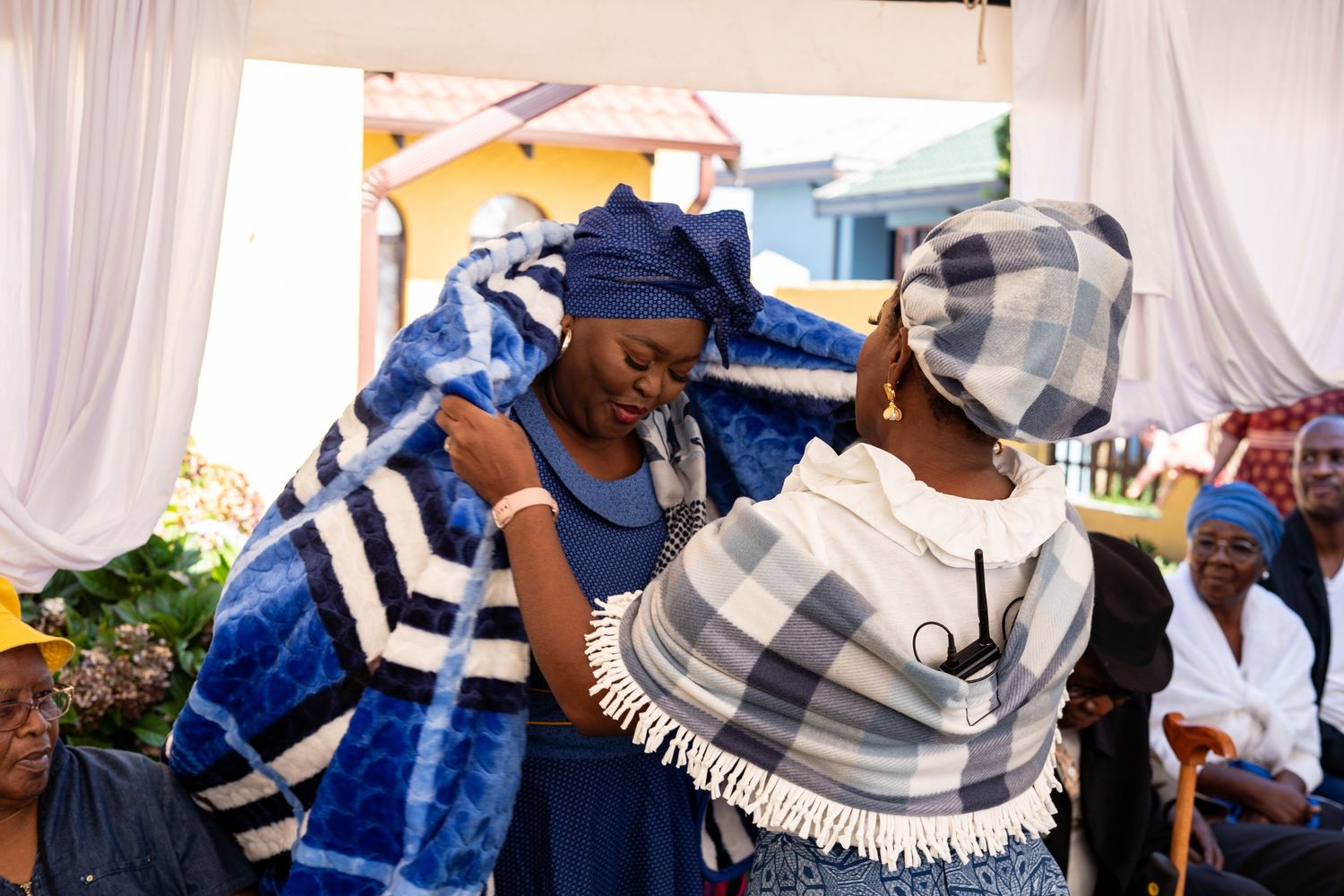 Women wrapping bride in traditional blue and white blanket during African traditional wedding ceremony.
