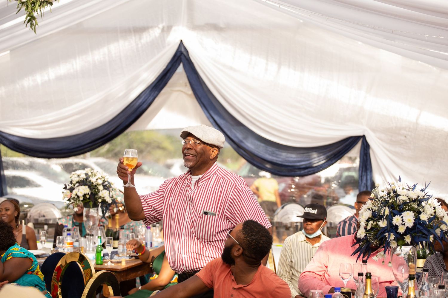 Man in pink striped shirt raising a glass in a toast at a decorated wedding reception venue.