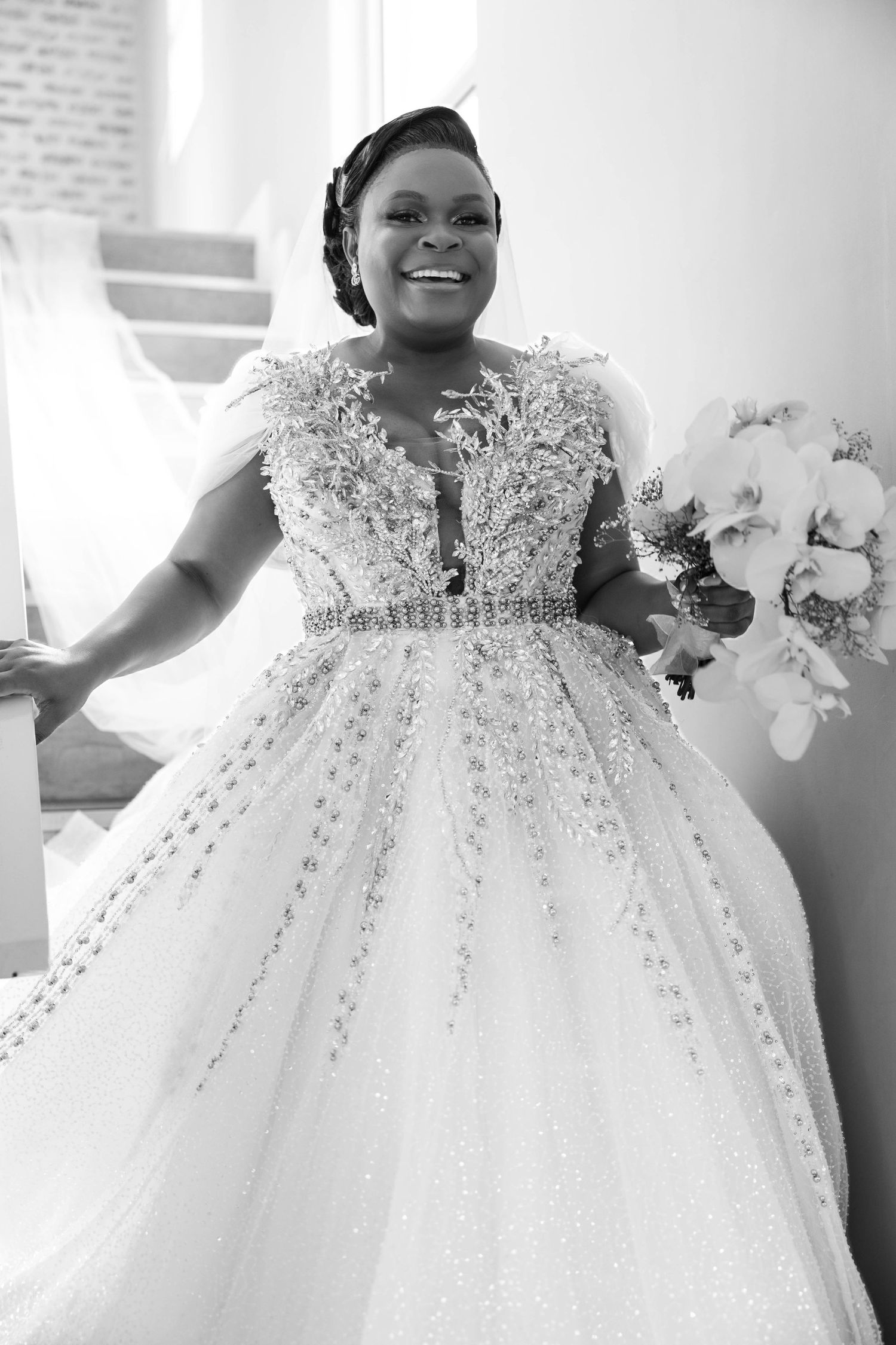 Black and white portrait of a smiling bride in a heavily beaded ball gown holding a white bouquet.