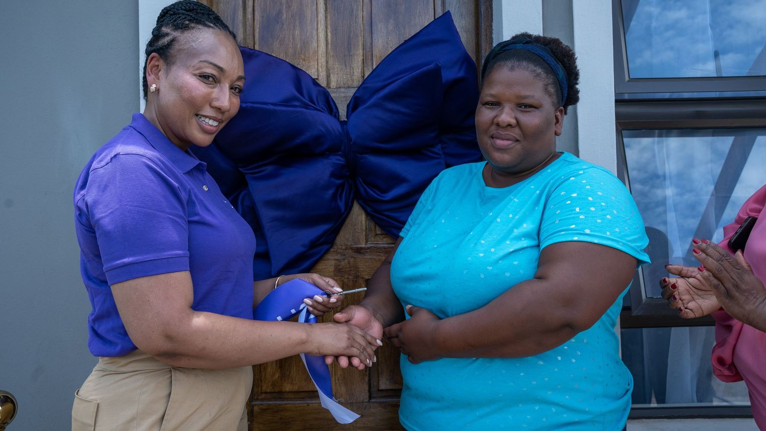 An Ithuba representative hands house keys to a smiling woman at a home handover event.