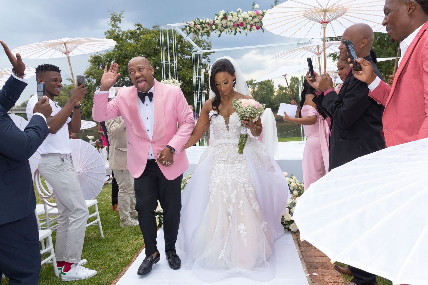 Joyful newlyweds walk down the aisle as guests celebrate at an elegant outdoor wedding ceremony.