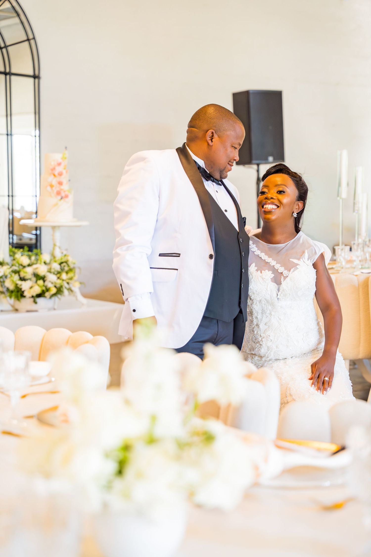 Bride and groom share a joyful moment beside elegantly decorated reception tables with floral centerpieces.