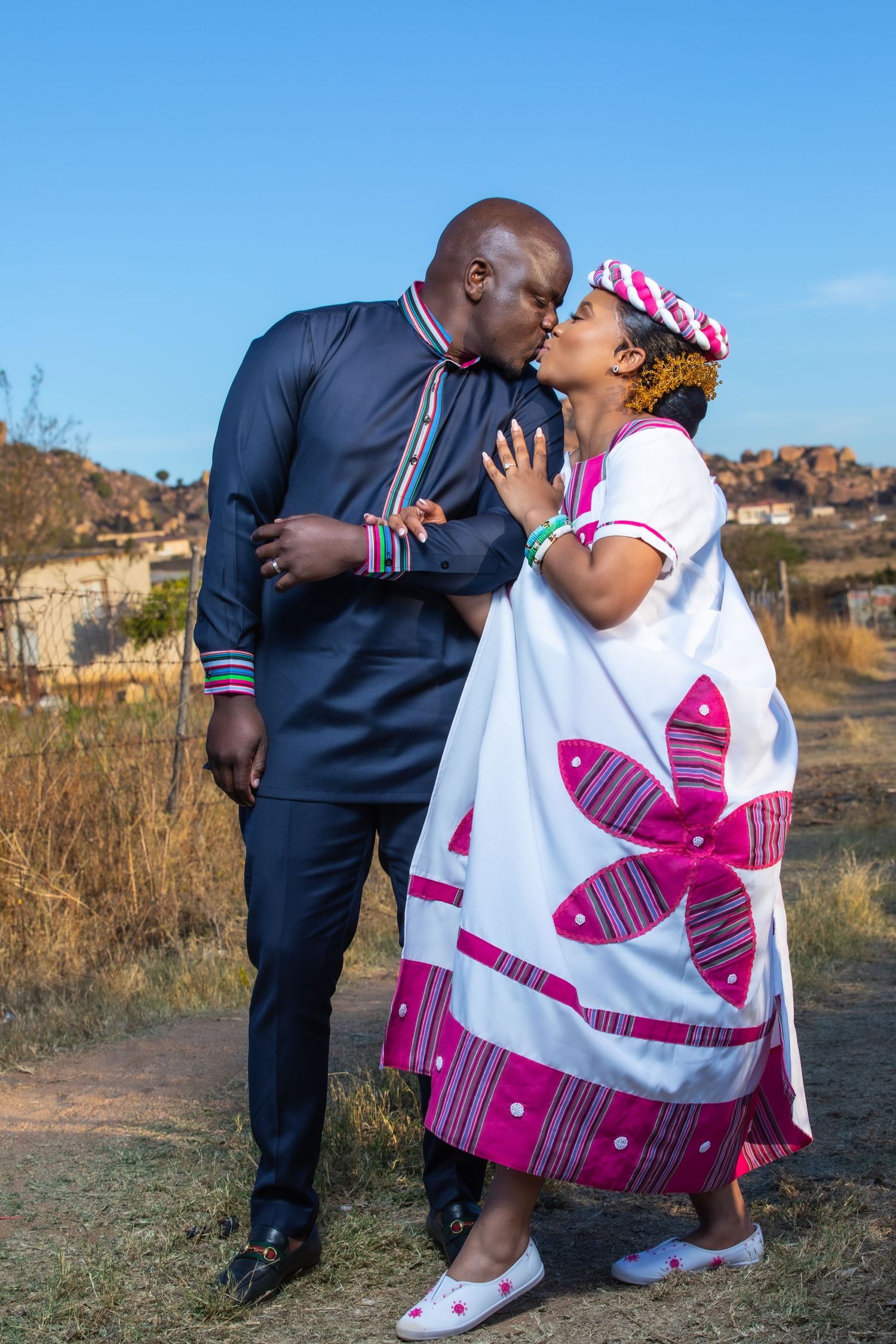African couple sharing a romantic kiss in traditional and formal wedding attire outdoors at sunset.