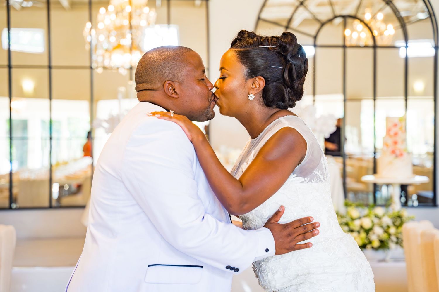 Bride and groom sharing a kiss at their wedding reception with floral decor in the background.