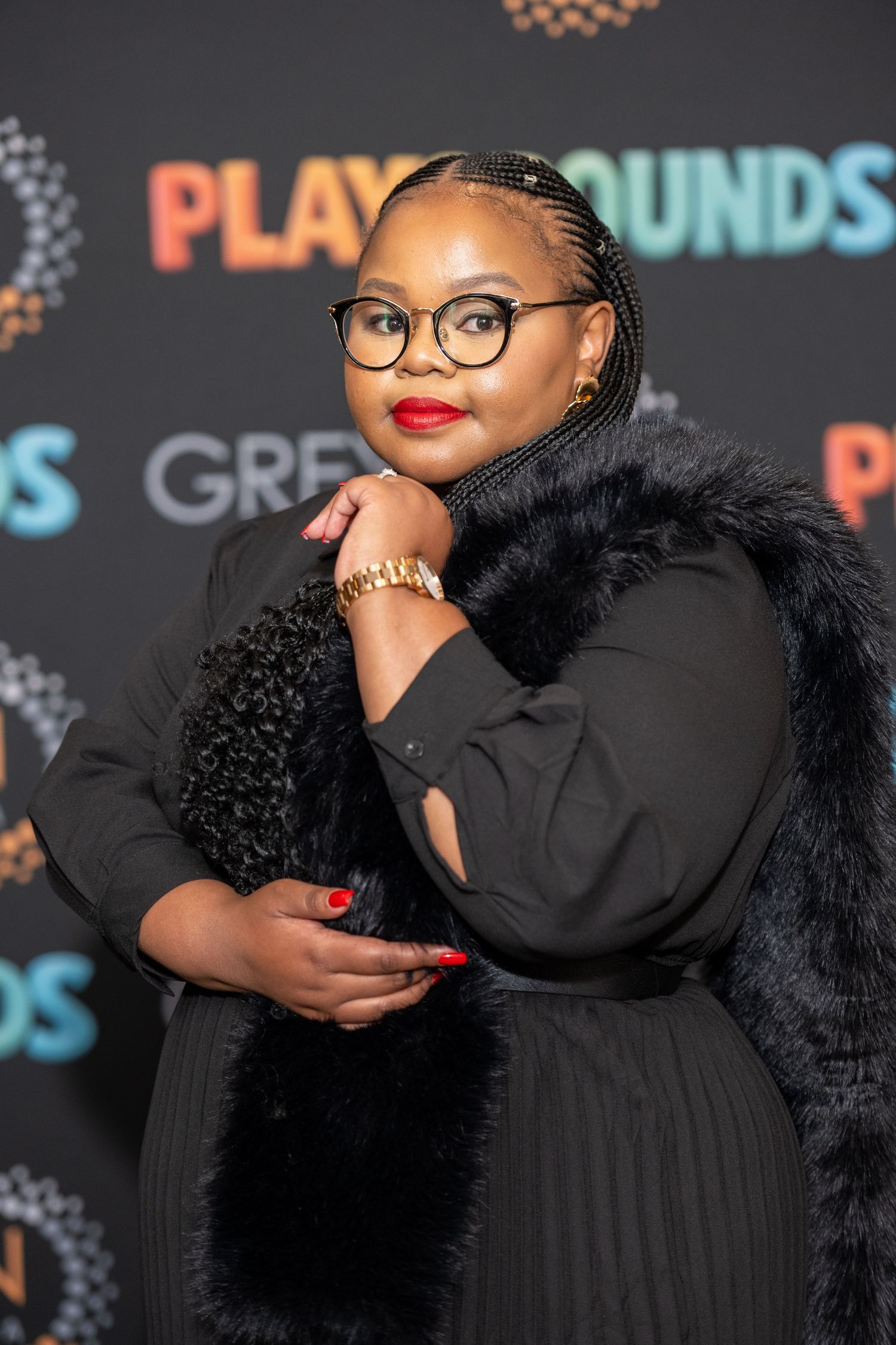 Woman in black outfit with fur trim and glasses poses at Playgrounds event.