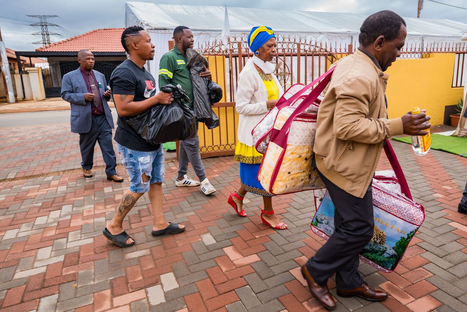 A group of people carrying bags and walking along a brick pathway during a traditional ceremony.