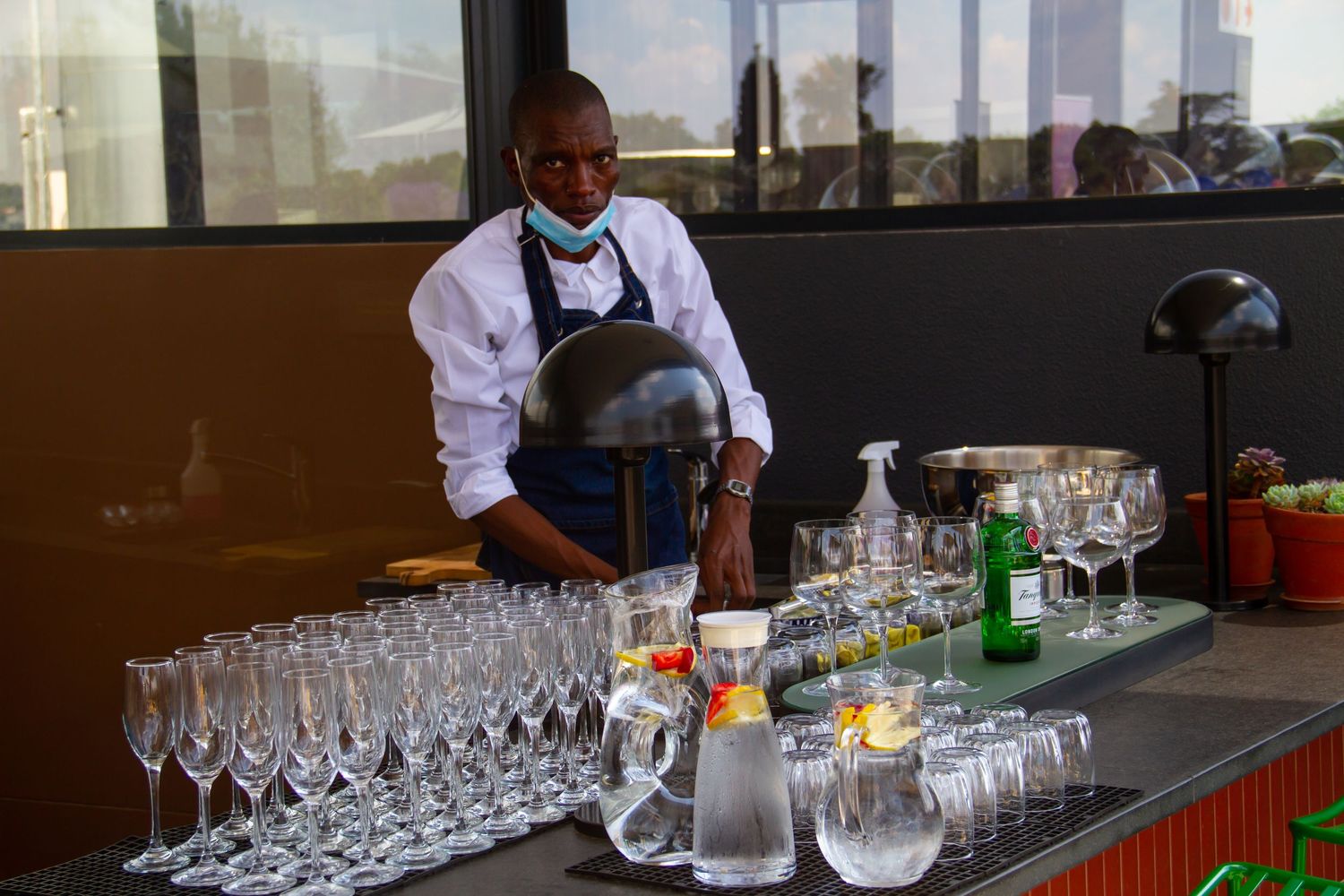 A catering staff member in a white uniform prepares champagne flutes and glassware at an event.