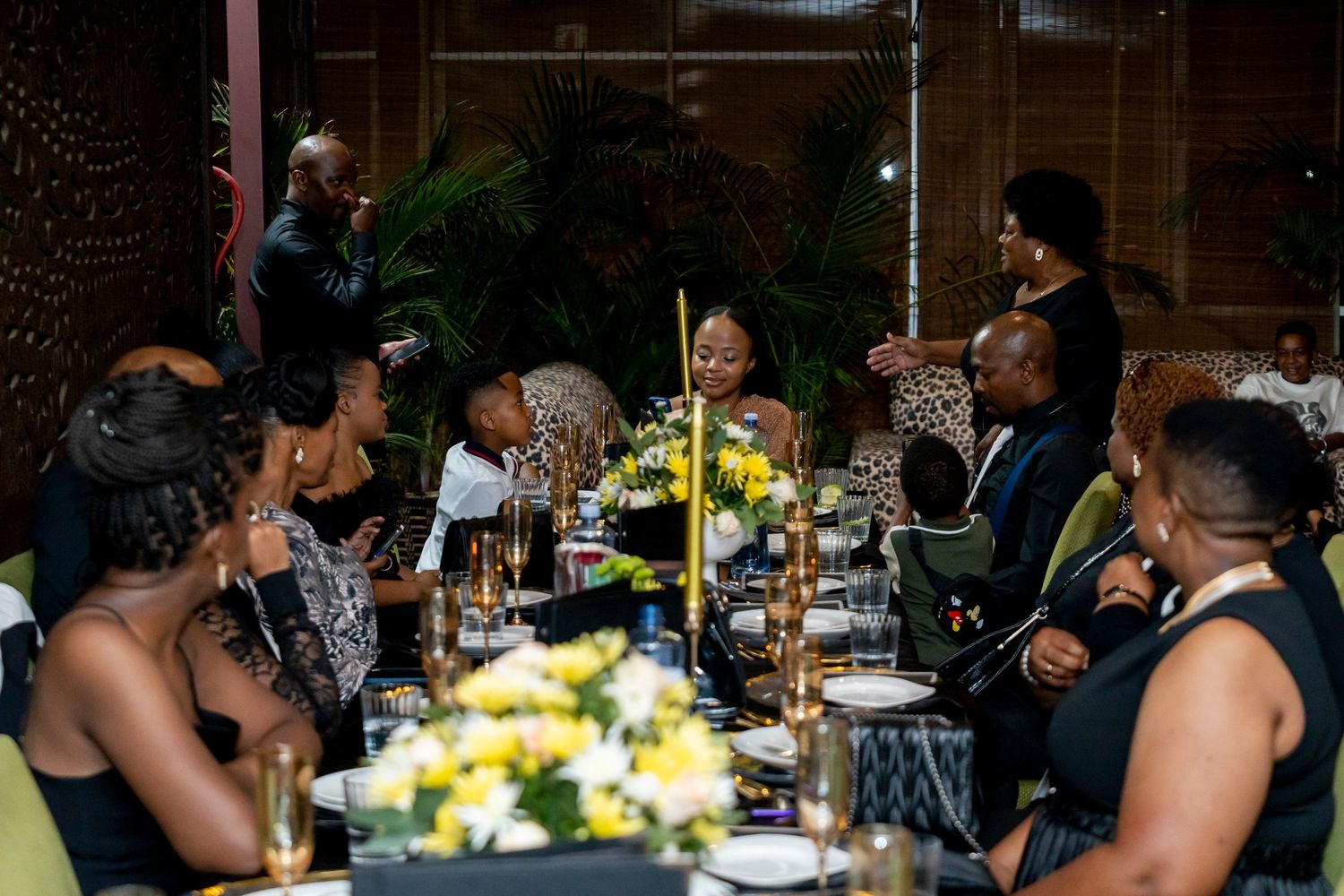 Guests gathered around decorated dinner table with yellow floral centerpiece at gala.