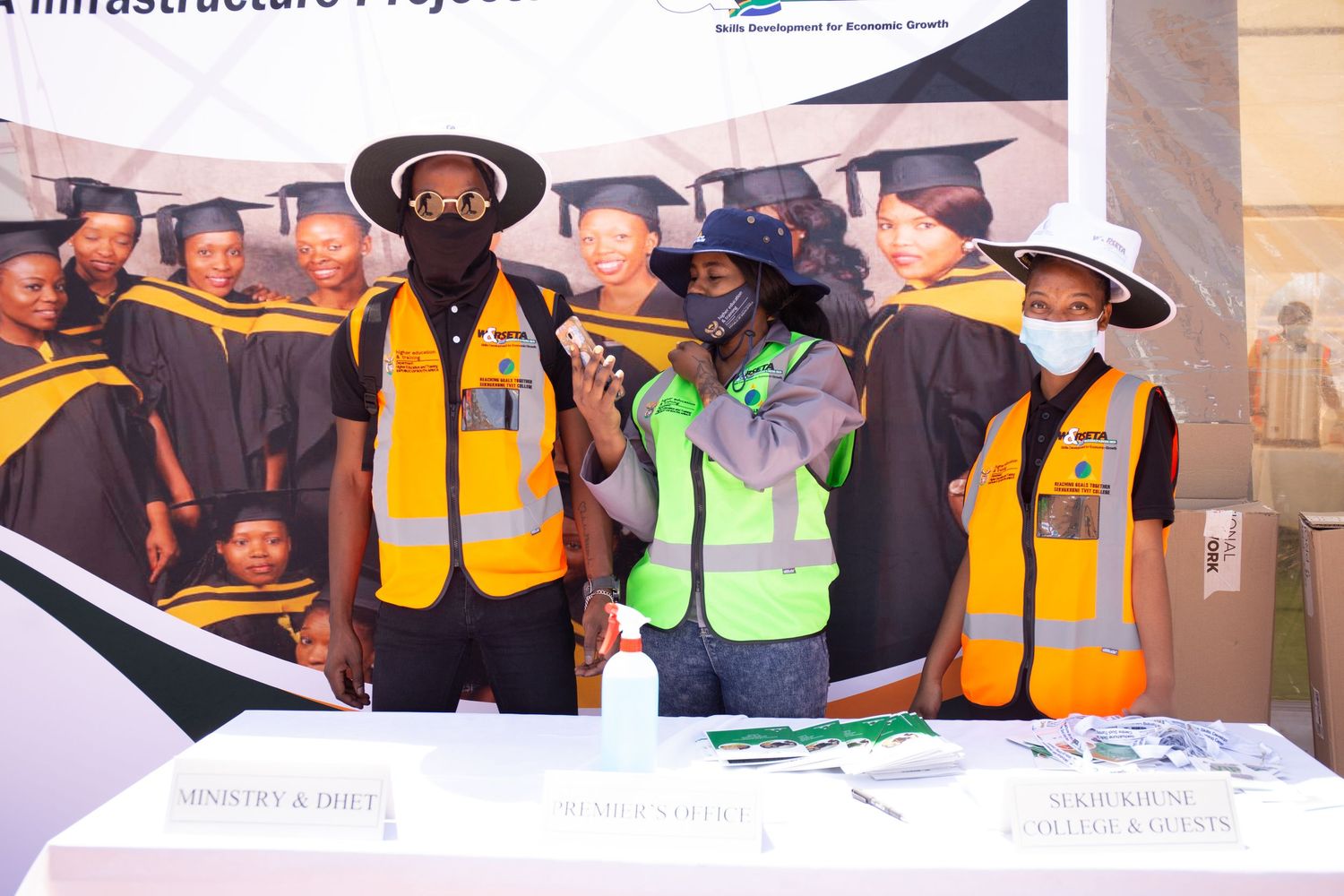 Workers in graduation gowns and safety vests participate in a skills development ceremony at a construction site.