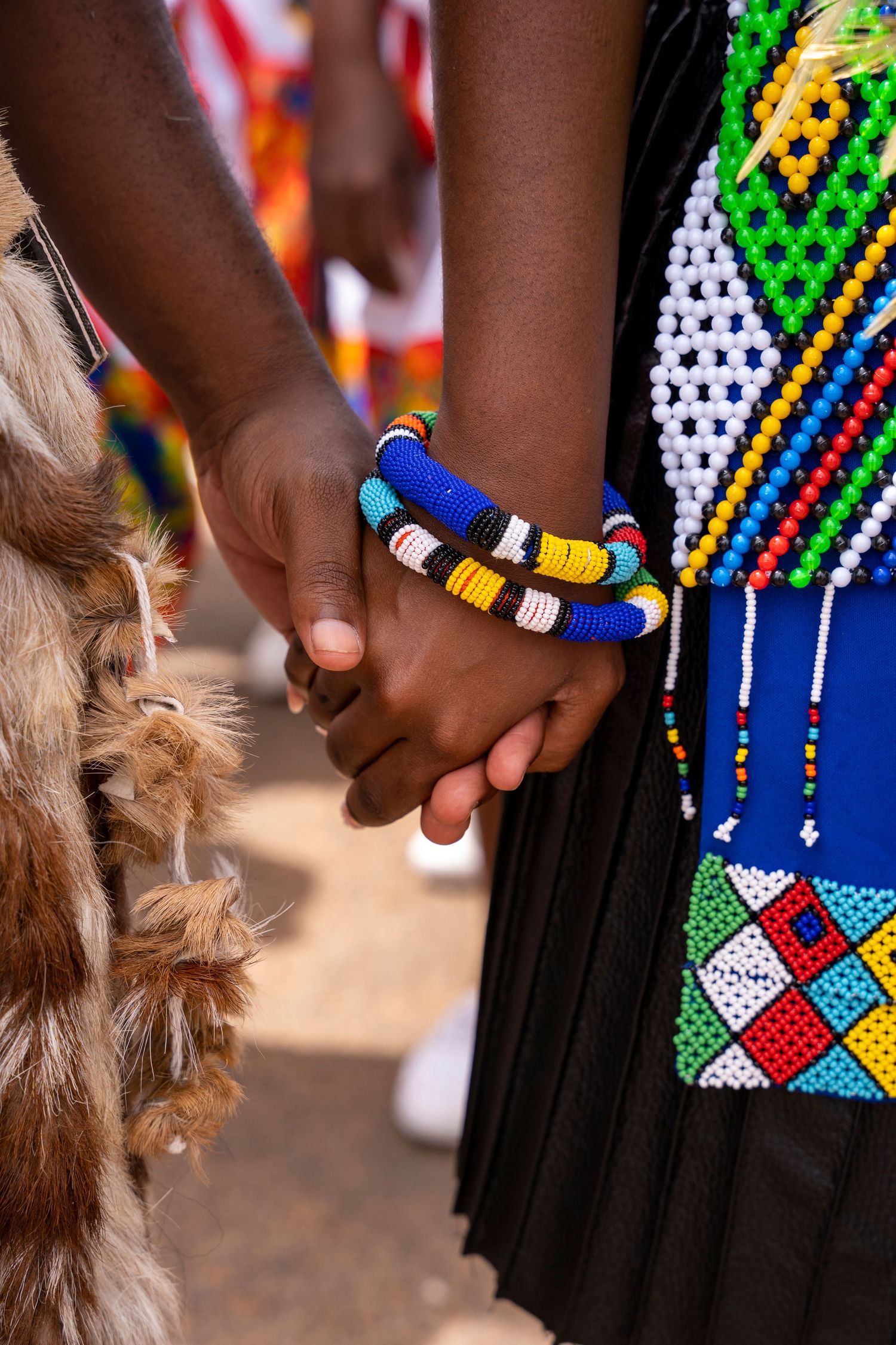 Close-up of couple holding hands wearing colorful Zulu beaded bracelets and traditional attire during cultural ceremony.