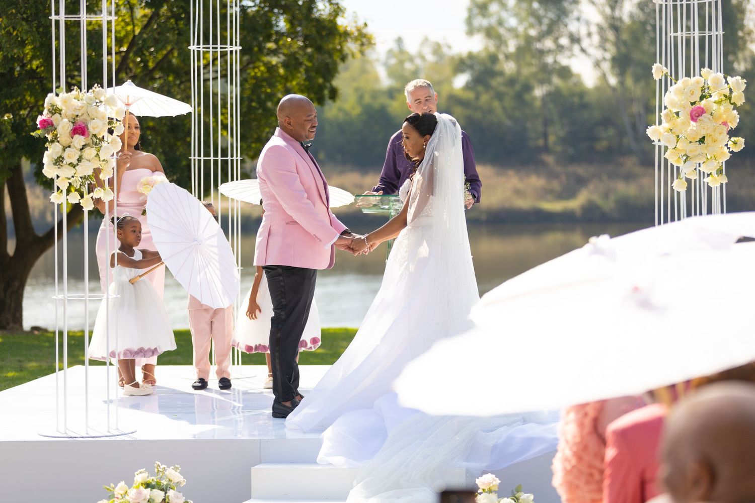 Bride and groom exchange vows at a stunning outdoor altar adorned with floral arrangements by a lake.