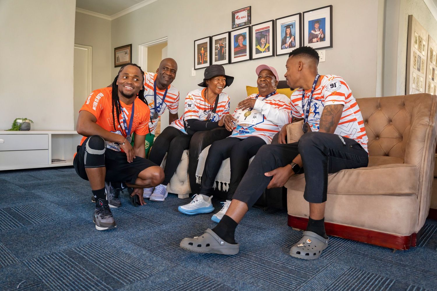 A group of five people smile together on a sofa wearing matching white and red striped shirts.
