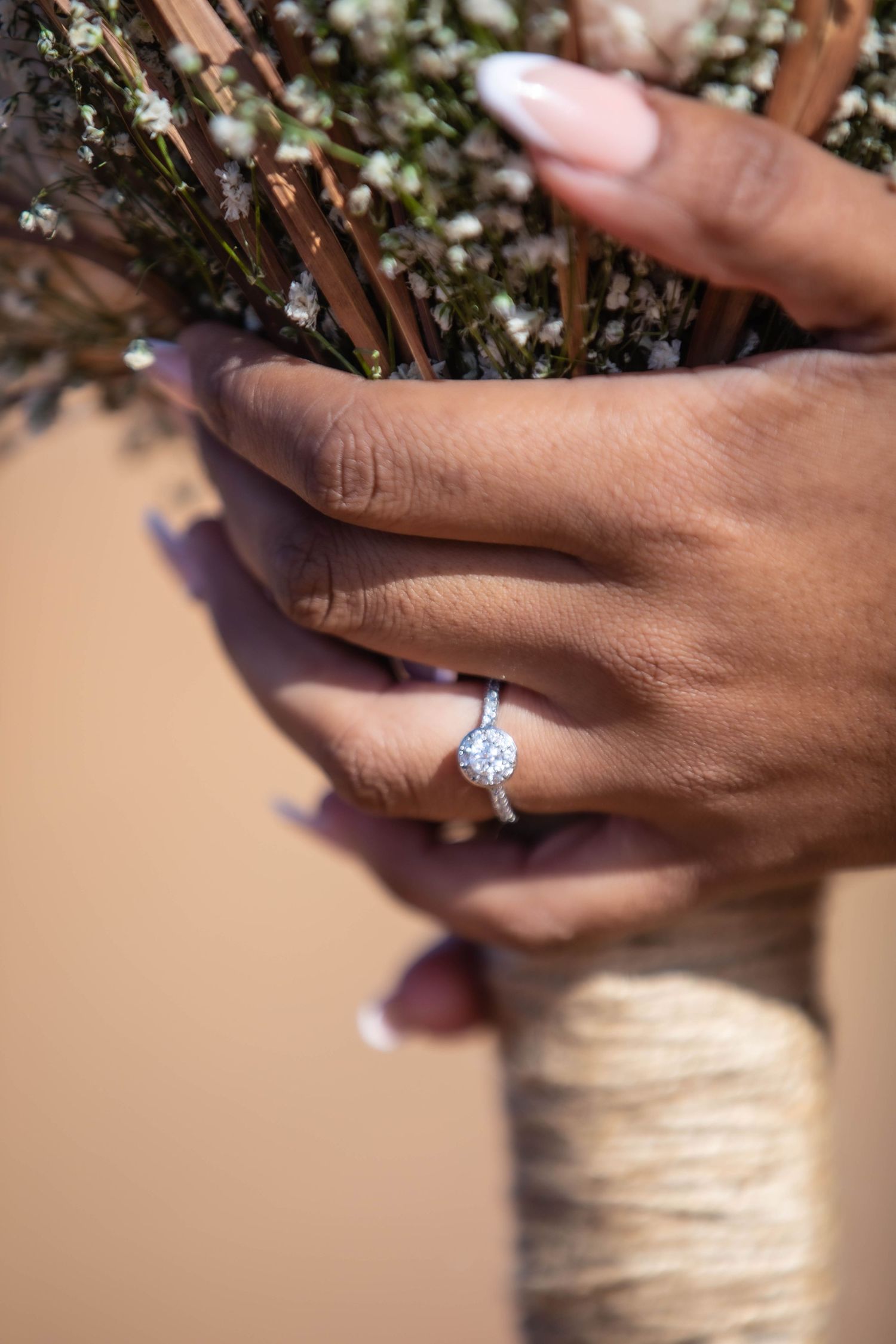 Close-up of diamond halo engagement ring on bride's hand holding rustic wedding bouquet.