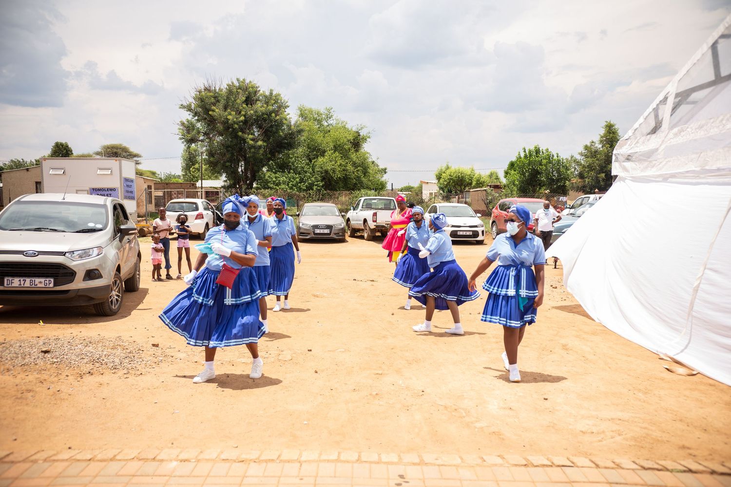 Women in traditional blue African attire performing a cultural dance outdoors at a wedding celebration.